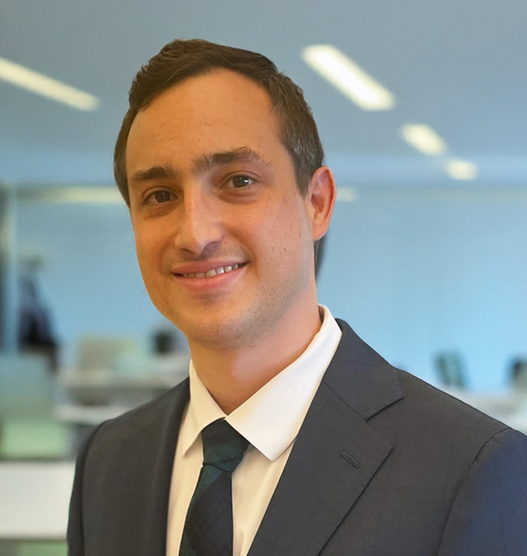 White male with dark hair in grey suit with white shirt and blue tie